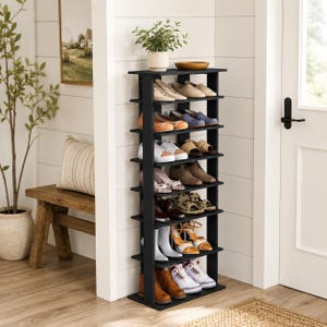 May include: A tall, narrow, black wooden shoe rack with eight horizontal shelves. The unit is filled with various types of footwear, including sneakers, boots, sandals, and dress shoes, arranged in pairs across the multiple levels of the storage rack.