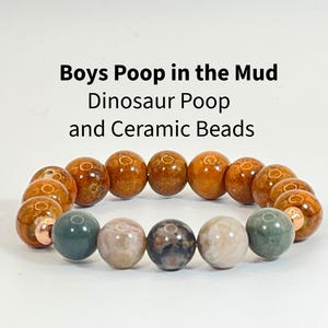 May include: A beaded bracelet featuring brown, tan, and green spherical beads with metallic copper-colored spacers. The text "Boys Poop in the Mud Dinosaur Poop and Ceramic Beads" is printed above the bracelet in black sans-serif font.