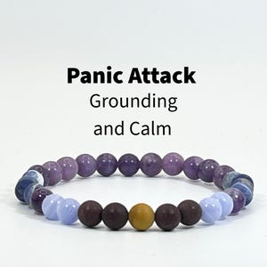 May include: A beaded bracelet featuring a variety of smooth, round stones in shades of purple, light blue, dark brown, and a single mustard yellow bead. Above the bracelet, the text reads: Panic Attack Grounding and Calm.
