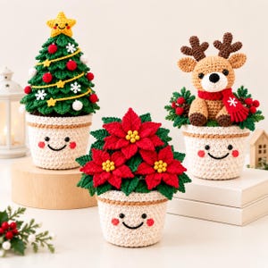May include: Three crocheted Christmas decorations in cream-coloured pots with smiling faces. One is a green tree with a yellow star, red and white ornaments. One is a red poinsettia plant. One is a brown reindeer wearing a red scarf.