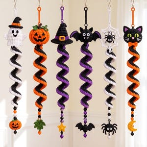 May include: Six hanging crochet decorations featuring Halloween themes including a ghost, pumpkin, witch hat, bat, spider web, and black cat. Each ornament has a long, spiraling tail in alternating colors and a small dangling charm at the bottom.