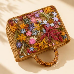 May include: A rectangular woven straw handbag featuring a vibrant floral pattern embroidered with colorful beads and sequins. The bag includes a curved bamboo handle attached with gold-tone metal hardware, showcasing a detailed botanical design.