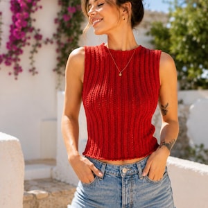 Puede incluir: Una camiseta sin mangas de punto acanalado rojo con cuello redondo y dobladillo recto, combinada con pantalones cortos de mezclilla azul claro con dobladillo deshilachado. La parte superior tiene un patrón texturizado vertical y cinco bolsillos.
