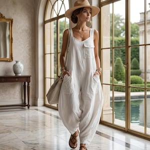 Könnte beinhalten: Weißer Leinen-Jumpsuit mit weiten Beinen und einer Vordertasche. Das Outfit wird mit braunen Sandalen, einem Strohhut und einer beigen Umhängetasche kombiniert. Der Jumpsuit hat eine lockere Passform, ideal für warmes Wetter.