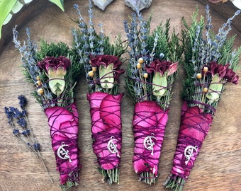 May include: Four bundles of dried herbs and flowers wrapped in pink rose petals and tied with twine. Each bundle has a silver charm with a crescent moon and a tree design.