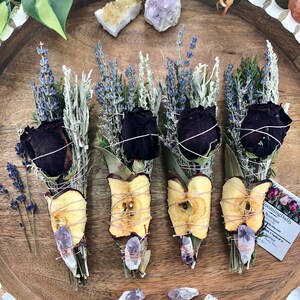 Op de afbeelding: Vier wierookstokjes met gedroogde appelschijfjes, lavendel, salie en cederhout. Elk wierookstokje is vastgebonden met touw en bevat een klein amethistkristal. De wierookstokjes zijn gerangschikt op een houten dienblad met extra amethistkristallen die eromheen zijn verspreid.