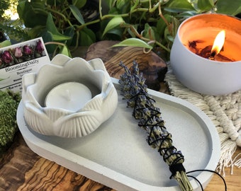 May include: A white ceramic tray with a lotus flower shaped candle holder and a bundle of dried lavender. The tray is on a wooden surface. BloomingDaily Boutique is written on a card in the background.