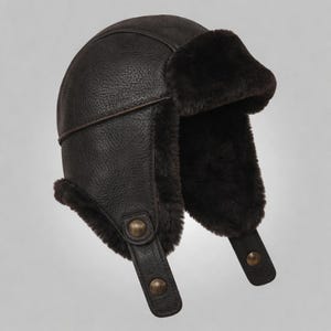 May include: A dark brown aviator hat with ear flaps and a faux fur lining. The hat features a leather exterior with a textured finish and adjustable chin straps with brass-colored buttons. The ear flaps are lined with dark brown faux fur.