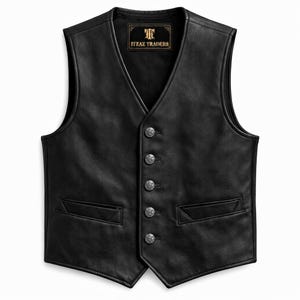 Op de afbeelding: Een zwart leren vest met een V-hals, vijf zilverkleurige decoratieve knopen en twee paspelzakken aan de voorzijde. Het binnenlabel toont de tekst ITZAZ TRADERS met een logo. Het kledingstuk heeft een gladde afwerking en een mouwloos ontwerp.