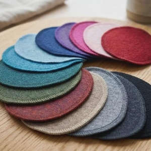 Puede incluir: Una colección de posavasos redondos y coloridos en varios tonos de azul, verde, rojo, rosa y gris. Los posavasos están dispuestos sobre una superficie de madera, mostrando sus diferentes tonos y texturas. Los posavasos están hechos de un material suave y absorbente.