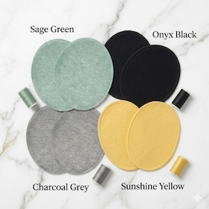Op de afbeelding: Een verzameling ronde stoffen pads in verschillende kleuren: saliegroen, onyx zwart, houtskoolgrijs en zonnegeel. Elk paar wordt vergezeld door een bijpassende spoel garen. De tekst geeft elke kleur aan.