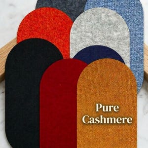 Könnte beinhalten: Eine Auswahl an halbkreisförmigen Kaschmir-Stoffmustern in verschiedenen Farben, darunter Schwarz, Rot, Orange, Marineblau, Grau und Blau. Der Text "Pure Cashmere" ist auf dem orangefarbenen Muster aufgedruckt. Die Muster sind auf einem Holzhalter angeordnet.