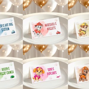 May include: A set of six white folded food tent cards featuring Paw Patrol characters. Each card displays a character, a colored watercolor splash, paw prints, a small vehicle icon, and text: Chase's Hot Dog Station, Marshall's Nuggets, Rubble's Mini Sandwiches, Rocky's Veggie Crunch, Skye's Pupcakes, and Zuma's Snack Boat.
