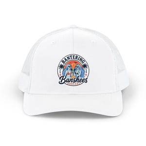 Op de afbeelding: Witte truckerpet met een mesh achterkant en een gebogen klep. De voorkant heeft een cirkelvormige afbeelding met de tekst "Bantering Banshees Podcast" en een illustratie van twee vrouwen met blauw haar en een zonnebril.
