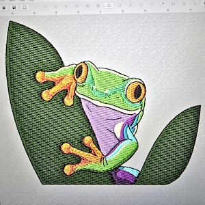 Op de afbeelding: Geborduurd ontwerp van een levendige groene boomkikker met oranje voeten en grote gele ogen, zittend op een donkergroen blad. De buik van de kikker is zachtpaars en de ledematen hebben blauwe en paarse accenten.