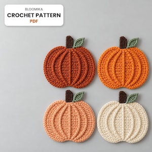 Könnte beinhalten: Vier gehäkelte Kürbis-Untersetzer in den Farben Dunkelorange, Hellorange, Pfirsich und Creme. Jeder Kürbis hat einen dunkelbraunen Stiel und ein kleines grünes Blatt. Der Text BLOOMIKA CROCHET PATTERN PDF ist in der oberen linken Ecke zu sehen.