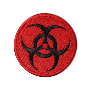 May include: A round, red patch with a black biohazard symbol in the center. The symbol is composed of three interlocking shapes. The patch has a stitched border.