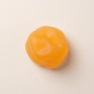 Può includere: Un singolo, luminoso peperone arancione su uno sfondo neutro. Il peperone ha una superficie liscia, leggermente lucida e una forma arrotondata con sottili creste. Il colore è un arancione vibrante e uniforme.
