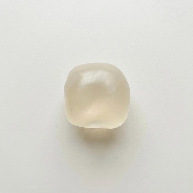 May include: A smooth, off-white, rounded object with a slightly translucent appearance. The object has a soft, organic shape and is set against a plain white background. The lighting creates subtle highlights and shadows.