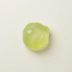 May include: A translucent, pale green, irregularly shaped object. The smooth, rounded form has a subtle gradient of color, transitioning from a lighter hue to a slightly deeper shade of green. The object is set against a neutral background.