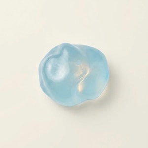 May include: A light blue, amorphous, organic-shaped object. The translucent form has a smooth, glossy surface and appears to be made of glass or resin. The object is set against a white background.