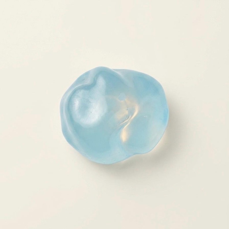 May include: A light blue, amorphous, organic-shaped object. The translucent form has a smooth, glossy surface and appears to be made of glass or resin. The object is set against a white background.