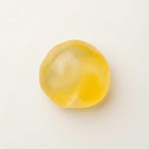 May include: A single, translucent, yellow, rounded object. The object has a smooth surface and a slightly irregular shape. The color is a warm, golden yellow, with variations in tone suggesting internal depth. The background is plain white.