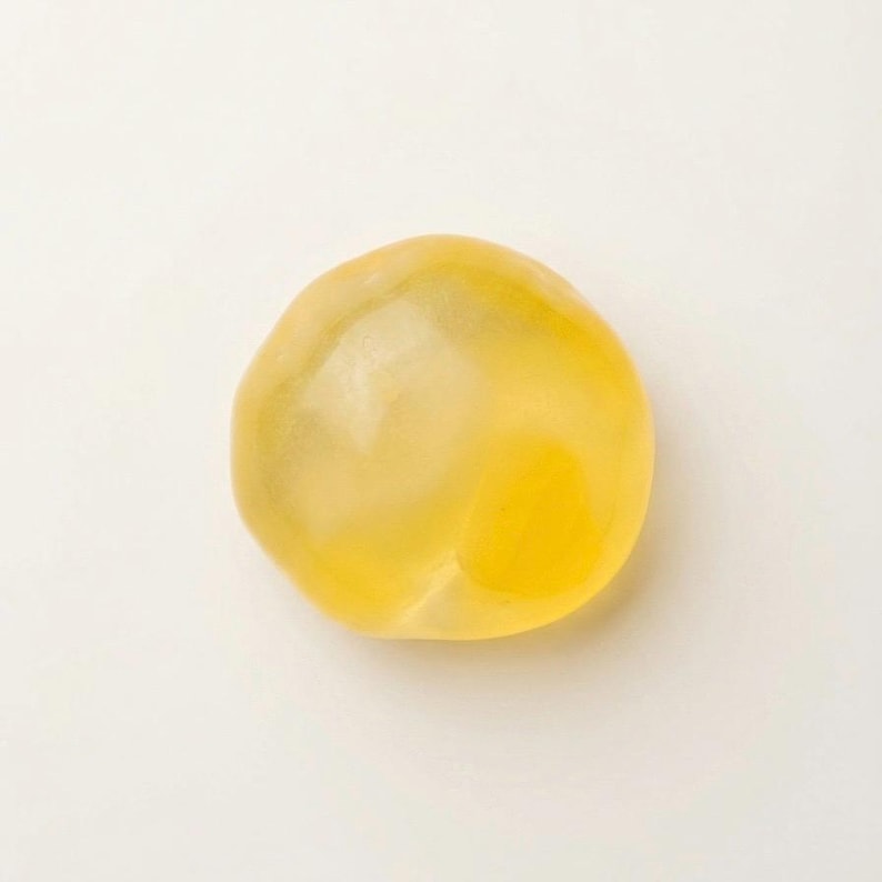 May include: A single, translucent, yellow, rounded object. The object has a smooth surface and a slightly irregular shape. The color is a warm, golden yellow, with variations in tone suggesting internal depth. The background is plain white.