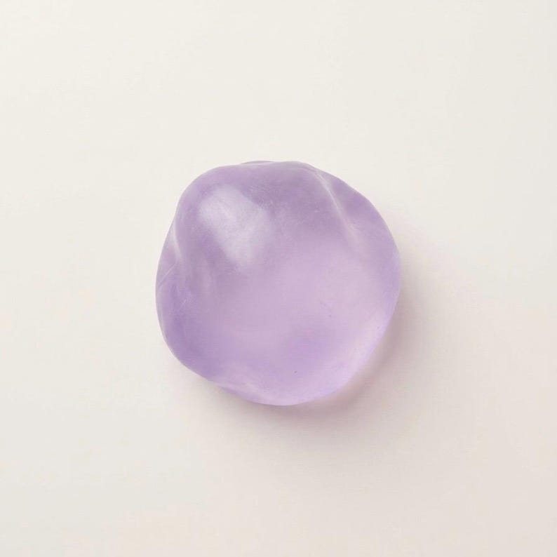 May include: A smooth, amorphous, lavender-colored object. The shape is irregular and rounded, with a slightly translucent appearance. The object is set against a plain, off-white background.
