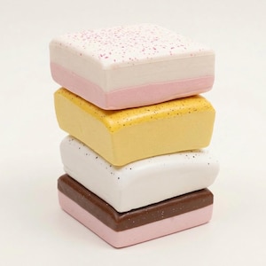 May include: A stack of four colorful, square-shaped objects. The top object is white with pink speckles and a pink base. Below it is a yellow object, then a white object, and finally a brown and pink object.
