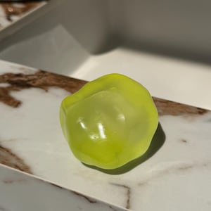 May include: A single, vibrant, lime-green bell pepper rests on a white and brown marble-patterned surface. The pepper has a smooth, glossy texture and is illuminated by natural light, creating highlights and shadows. The image is a close-up, showcasing the pepper's shape and color.