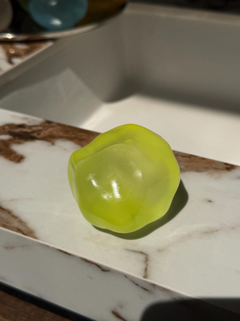 May include: A single, vibrant, lime-green bell pepper rests on a white and brown marble-patterned surface. The pepper has a smooth, glossy texture and is illuminated by natural light, creating highlights and shadows. The image is a close-up, showcasing the pepper's shape and color.