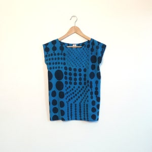 May include: A blue and black polka dot patterned shirt with short sleeves. The shirt is hanging on a wooden hanger against a white background.