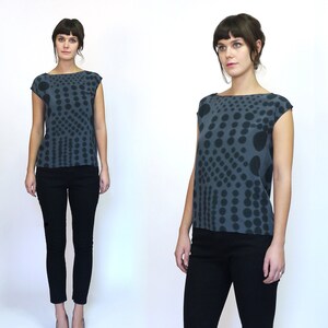 May include: Two women wearing grey and black patterned tops with black trousers. The tops have a scoop neck and short sleeves. The pattern is a mix of small and large black dots on a grey background.