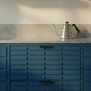 May include: A stainless steel gooseneck kettle with a black handle sits on a concrete countertop. Below, dark blue kitchen cabinets with black handles provide storage. The kitchen design has a modern aesthetic.