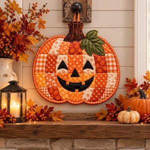 May include: A quilted fabric wall hanging shaped like a jack-o'-lantern pumpkin, featuring a patchwork design of orange, red, and white floral and gingham patterns. It has a dark brown stem, a green leaf, and a black stitched face with eyes and a mouth.