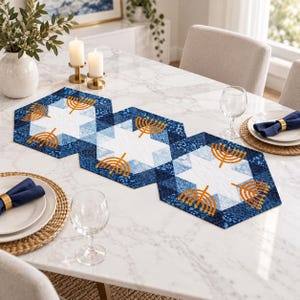 May include: A quilted table runner featuring a geometric pattern of blue and white hexagons. The design includes repeating gold-coloured menorah motifs printed across the fabric. The runner is composed of three connected hexagonal sections.