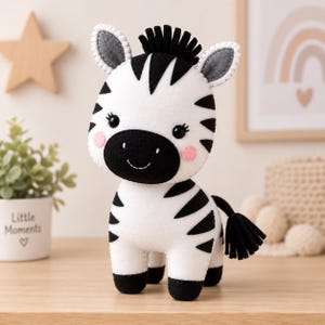May include: A plush zebra toy made of white felt with black felt stripes, a black mane, and a black tail. The zebra features a black muzzle, pink circular cheeks, and black embroidered eyes with eyelashes, standing on four black felt hooves.