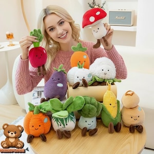 Puede incluir: Colección de peluches de verduras, que incluyen un rábano rojo, una zanahoria naranja, una berenjena morada y una coliflor blanca. Cada juguete tiene una cara sonriente y pies marrones. También hay un peluche de seta roja y blanca.