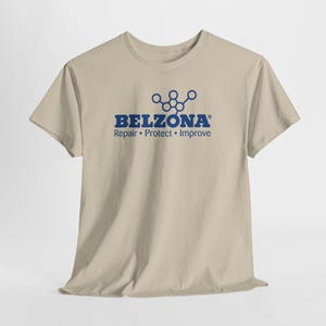 Può includere: Una t-shirt beige a maniche corte con una grafica blu sul petto. La grafica mostra la parola BELZONA in grassetto maiuscolo, un'icona di struttura molecolare sopra e il testo Repair • Protect • Improve stampato al di sotto.
