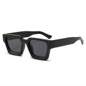 Puede incluir: Gafas de sol cuadradas negras con lentes oscuras. Las gafas tienen una montura y patillas gruesas y atrevidas. Las lentes son de color gris oscuro y la montura es negra lisa. Las gafas son de estilo moderno.