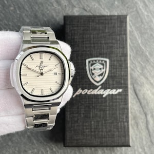 May include: A silver wristwatch with a white face and a matching metal strap. The watch features a rectangular face with a textured pattern and a date display. The watch is next to a black box with the brand name "poedagar".