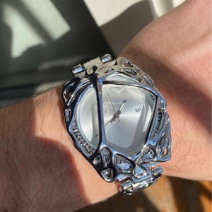 May include: A silver-toned wristwatch with a unique, openwork design around the face and band. The watch face is a light silver color with silver hands and markers. The watch is worn on a wrist.