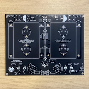 Może przedstawiać: Czarna płytka drukowana z białymi liniami schematycznymi i tekstem. Płytka zawiera różne kontury elementów elektronicznych, w tym okręgi, kwadraty i kształty rombów. Tekst zawiera ostrzeżenie dotyczące tranzystorów i numer wersji płytki.