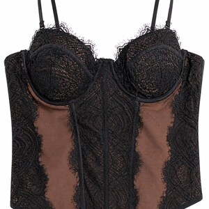 May include: Black lace bustier with adjustable straps. The bustier features a sheer brown panel in the center and sides, with intricate lace detailing and scalloped edges. A classic lingerie piece.