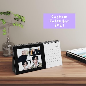 May include: A desk calendar for May 2027 with a black spiral binding. The left side features three photographic portraits of a person with dark hair, while the right side displays the calendar grid for May. A purple graphic reads Custom Calendar 2027.