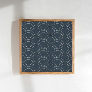 May include: Square framed artwork featuring a navy blue pattern of overlapping, stitched semi-circles. The design is set against a textured background, with a light-colored wooden frame. The artwork has a minimalist, geometric aesthetic.