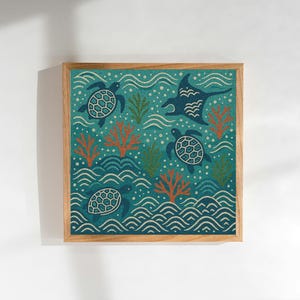 May include: Square framed art print featuring an ocean scene with teal turtles, a manta ray, coral, and stylized waves. The artwork has a textured appearance and is set against a teal background. The frame is made of light-colored wood.