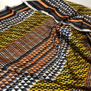 May include: Black and white fabric with a geometric pattern of triangles in shades of yellow, orange, and gray. The fabric is folded and draped, showing the pattern from different angles.