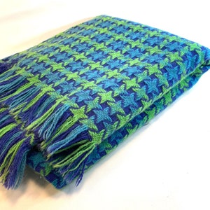 May include: A folded blue and green throw blanket with a star pattern and fringe on the edges.